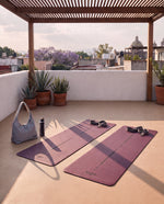 Dos tapetes de yoga Serenity color vino desenrollados en una azotea, con la bolsa y el termo ioga del pack