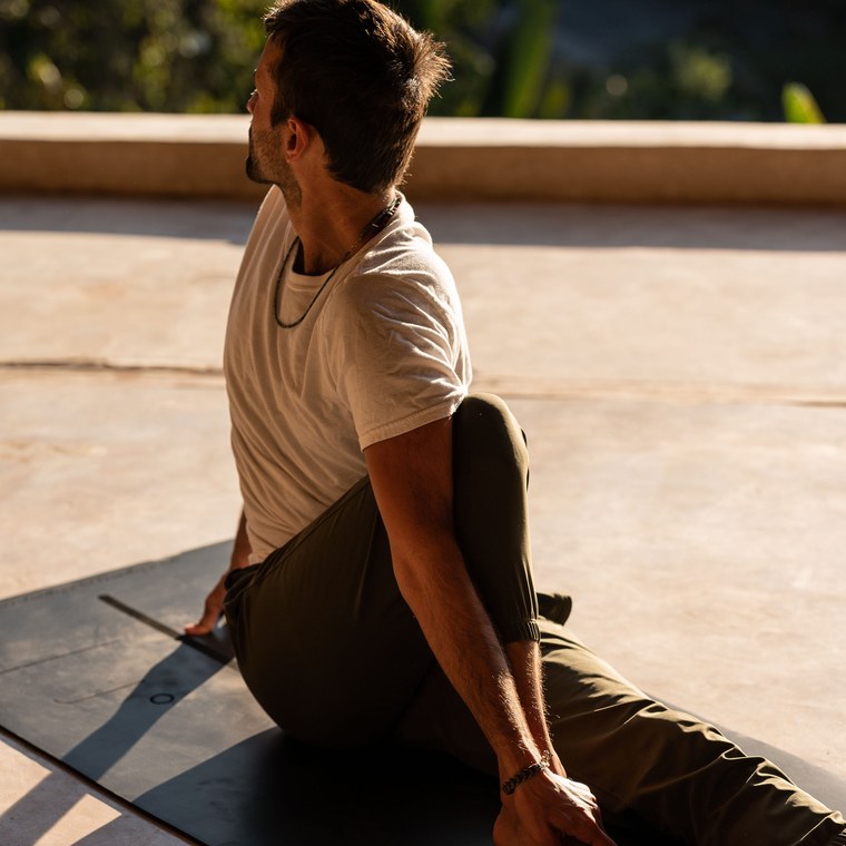 Hombre practicando torsión sentada de yoga sobre tapete IOGA de caucho natural