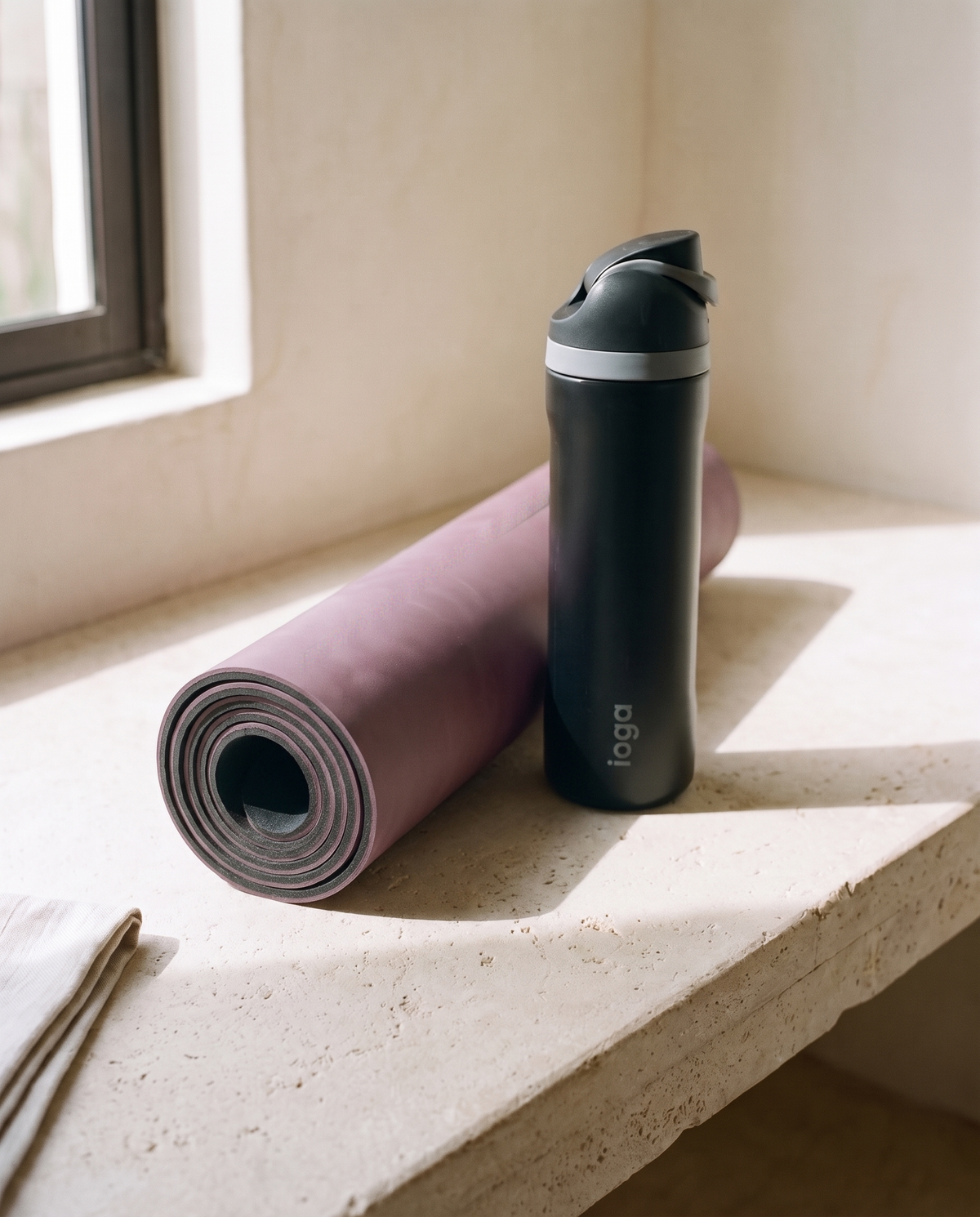 Serenity Mat de ioga enrollado junto al termo ioga 710 ml de regalo sobre una banca de cantera